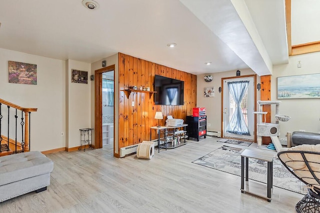 living area with wood walls, stairway, a baseboard heating unit, baseboards, and wood finished floors