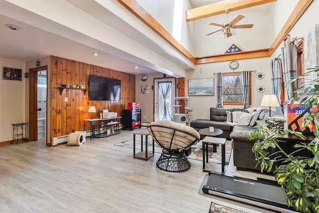 living area featuring wood finished floors, wood walls, a towering ceiling, a ceiling fan, and baseboard heating