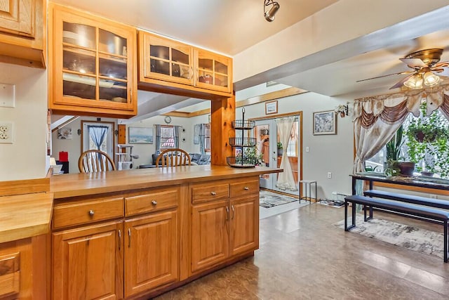 kitchen with a ceiling fan, glass insert cabinets, brown cabinetry, wood counters, and a baseboard heating unit