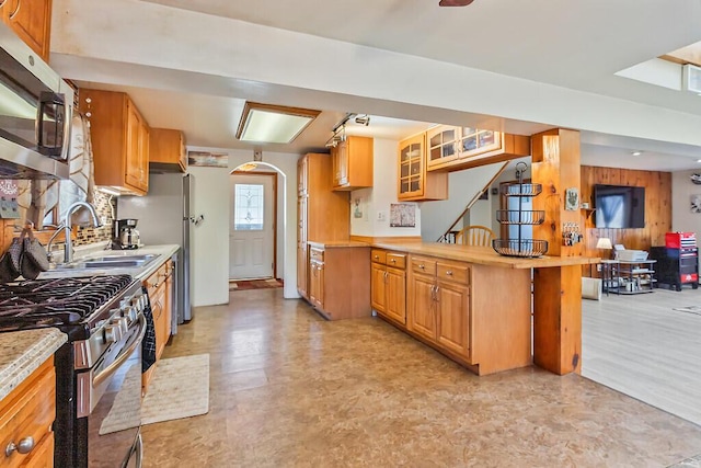 kitchen with light countertops, a sink, a peninsula, glass insert cabinets, and stainless steel appliances