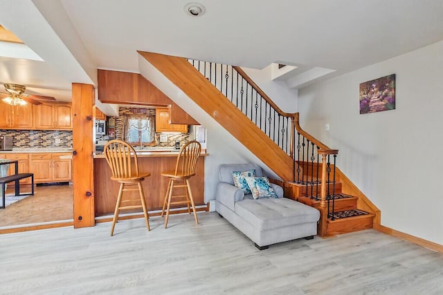 living room featuring baseboards, light wood-style flooring, stairway, and a ceiling fan