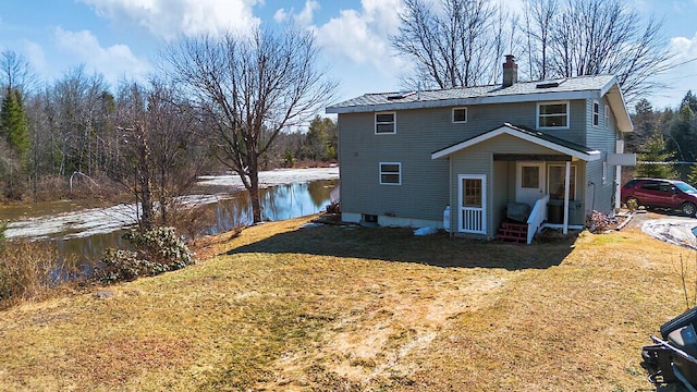 rear view of property with a lawn, a chimney, and a water view
