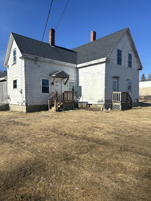 back of property with a deck, roof with shingles, and a chimney