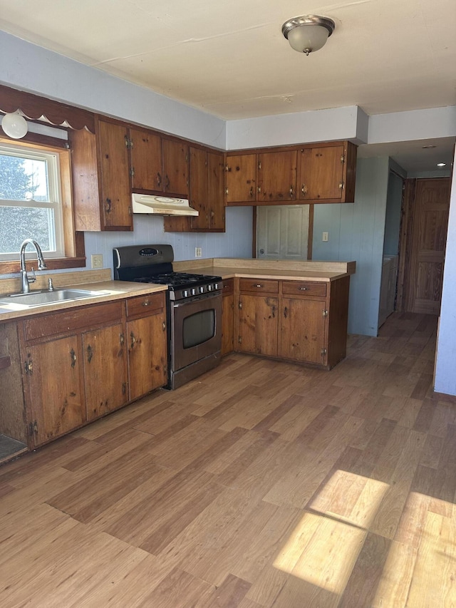 kitchen featuring under cabinet range hood, brown cabinets, stainless steel gas range, and a sink