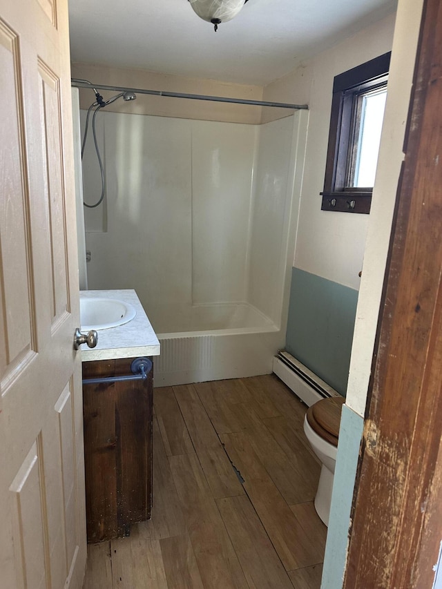 bathroom with toilet, vanity, wood finished floors, washtub / shower combination, and a baseboard radiator