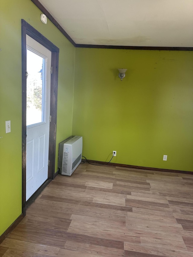 empty room with heating unit, baseboards, light wood finished floors, and ornamental molding