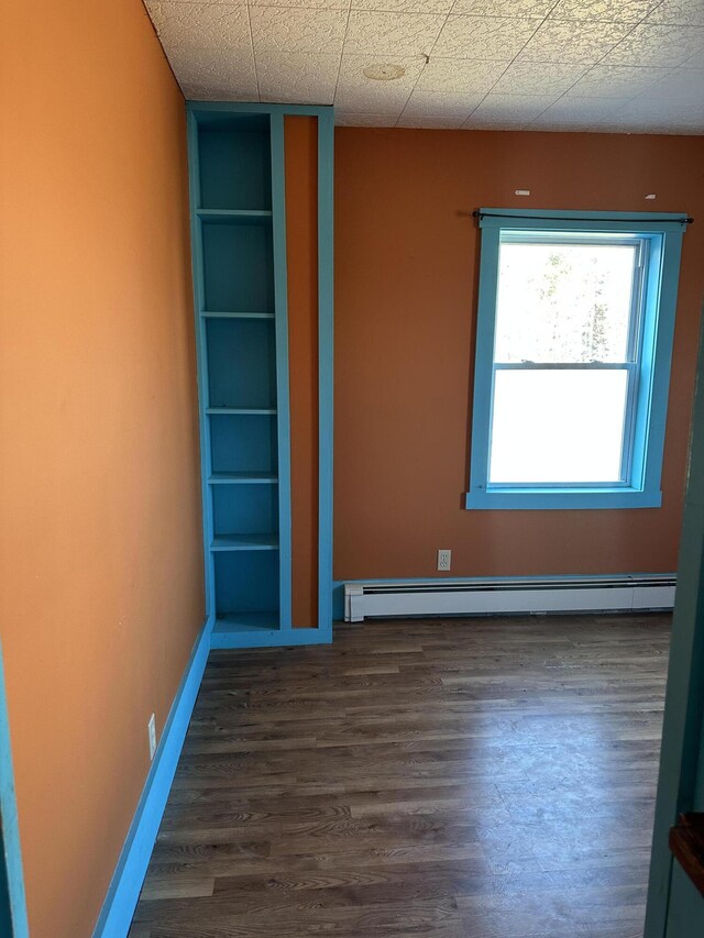 spare room with a baseboard heating unit, baseboards, and wood finished floors