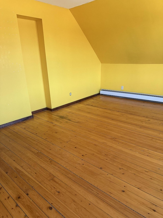 additional living space featuring a baseboard heating unit, lofted ceiling, baseboards, and hardwood / wood-style floors