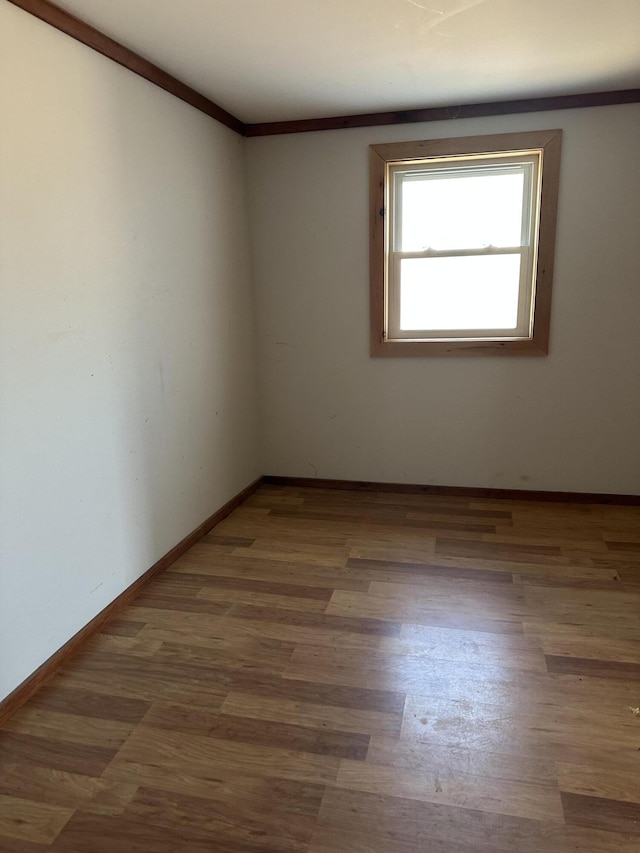 empty room featuring baseboards, wood finished floors, and ornamental molding