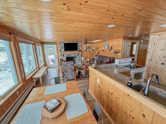 kitchen featuring wood finished floors, a stone fireplace, a baseboard heating unit, wooden ceiling, and white electric range