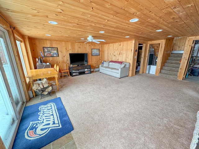 unfurnished living room featuring wood walls, stairs, carpet flooring, wooden ceiling, and a ceiling fan