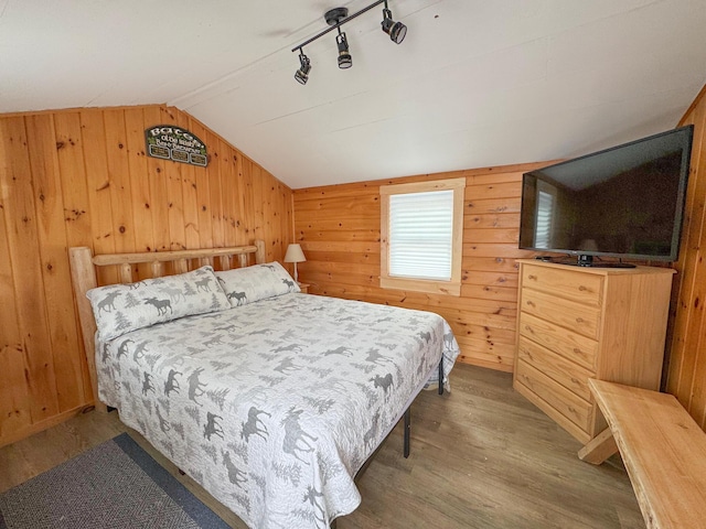 bedroom with lofted ceiling, wooden walls, wood finished floors, and track lighting