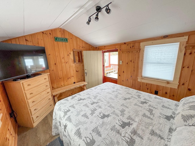 bedroom featuring wood walls, rail lighting, and vaulted ceiling