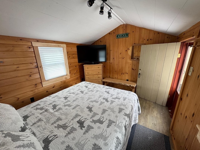 bedroom featuring vaulted ceiling, wood finished floors, wood walls, and track lighting