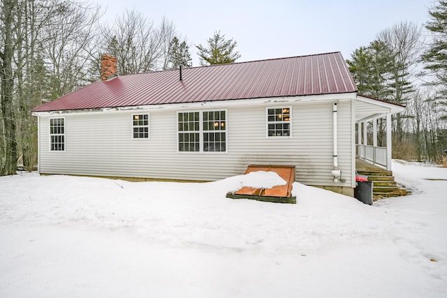 snow covered rear of property with metal roof and a chimney