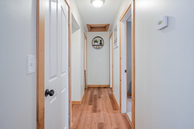 hall with attic access, light wood-style floors, and baseboards