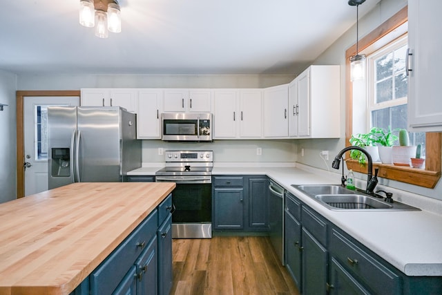 kitchen featuring butcher block countertops, a sink, wood finished floors, appliances with stainless steel finishes, and white cabinets