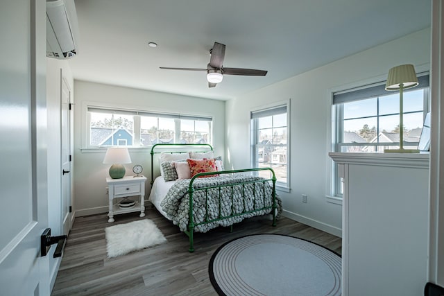 bedroom featuring ceiling fan, an AC wall unit, baseboards, and wood finished floors