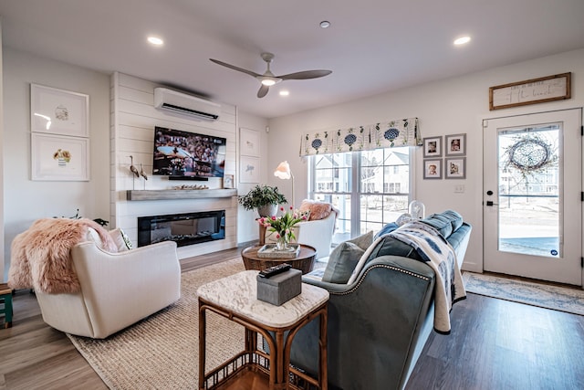 living room featuring a glass covered fireplace, a healthy amount of sunlight, an AC wall unit, and wood finished floors