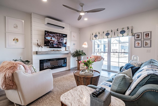 living area featuring ceiling fan, a wall mounted air conditioner, recessed lighting, wood finished floors, and a glass covered fireplace