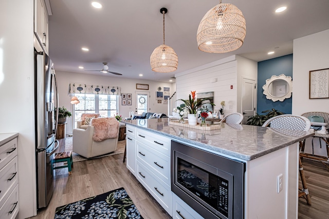 kitchen featuring open floor plan, a kitchen bar, light wood-style flooring, stainless steel appliances, and white cabinetry