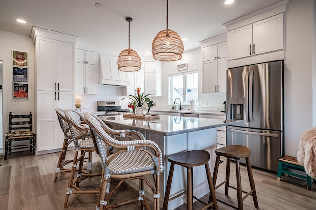 kitchen with light wood finished floors, white cabinetry, appliances with stainless steel finishes, a kitchen bar, and a center island