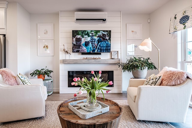 living room featuring a glass covered fireplace, a wall mounted AC, and wood finished floors