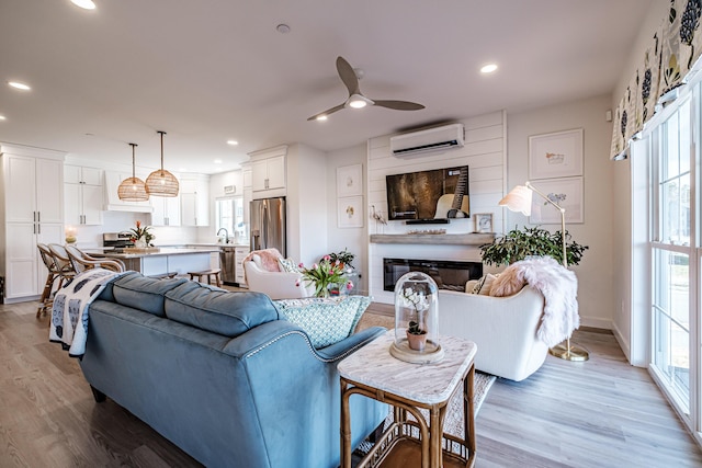 living area featuring a glass covered fireplace, light wood finished floors, recessed lighting, and a wall mounted air conditioner