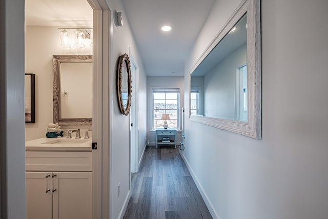 hallway with recessed lighting, wood finished floors, baseboards, and a sink