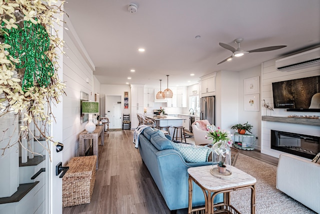 living area featuring ceiling fan, an AC wall unit, recessed lighting, wood finished floors, and a glass covered fireplace