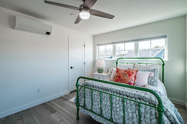 bedroom with a wall mounted air conditioner, baseboards, wood finished floors, and a ceiling fan