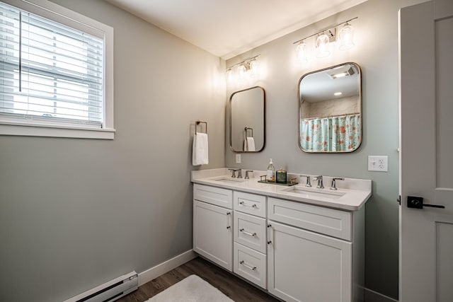 full bath featuring a sink, a baseboard heating unit, wood finished floors, and double vanity