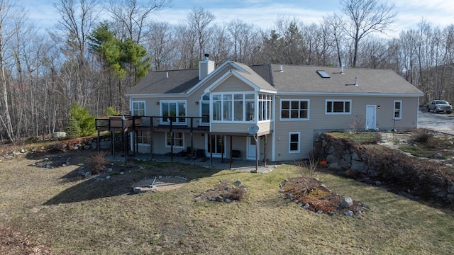 rear view of house with a wooden deck, a patio, a chimney, a sunroom, and a lawn