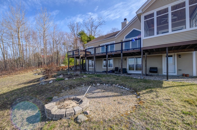 rear view of property with a chimney, a yard, a fire pit, and a deck