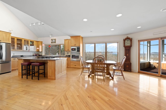 kitchen with glass insert cabinets, appliances with stainless steel finishes, a kitchen island, and light wood-type flooring