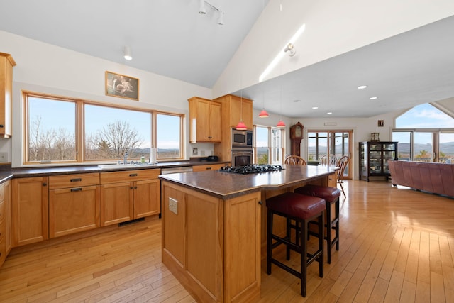 kitchen featuring a kitchen bar, dark countertops, a center island, light wood-type flooring, and stainless steel appliances
