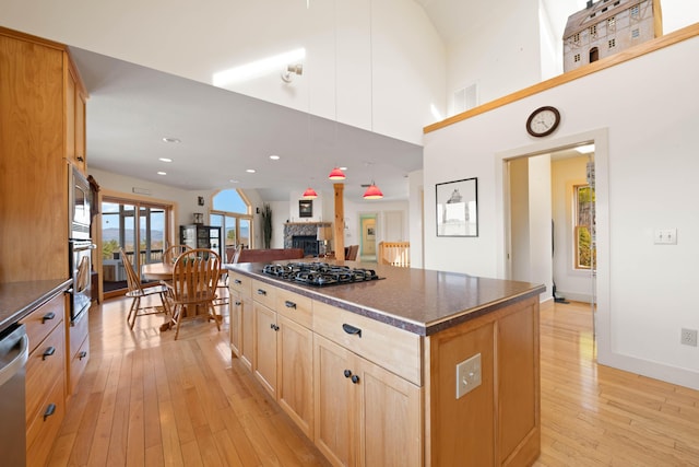 kitchen featuring light brown cabinetry, dark countertops, light wood-style floors, a stone fireplace, and stainless steel appliances