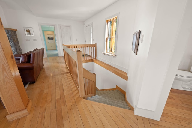 hallway featuring light wood-style floors, baseboards, and an upstairs landing
