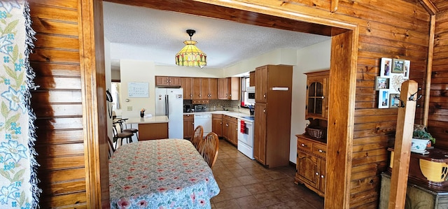 kitchen featuring decorative backsplash, brown cabinets, white appliances, light countertops, and decorative light fixtures