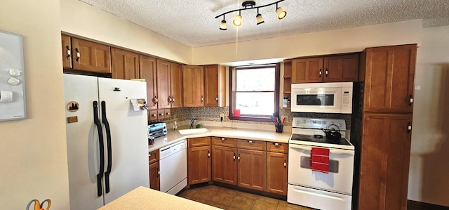 kitchen featuring brown cabinets, a sink, white appliances, and a textured ceiling