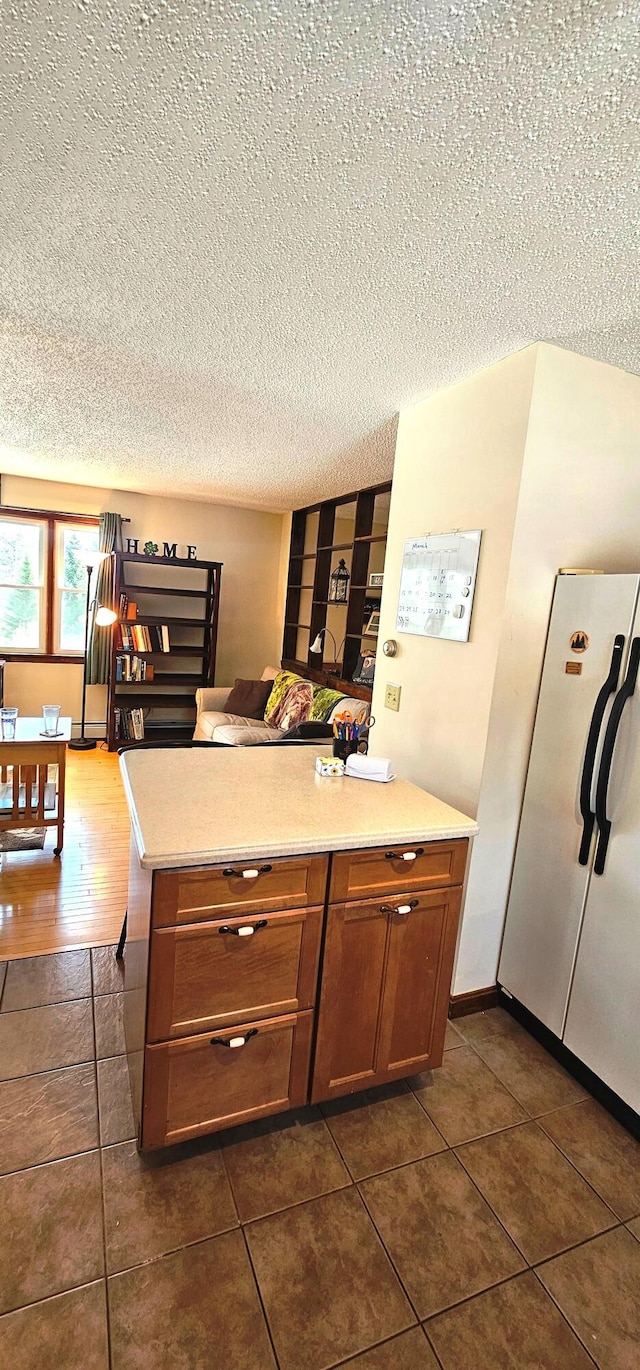 kitchen featuring light countertops, freestanding refrigerator, a textured ceiling, and dark tile patterned flooring