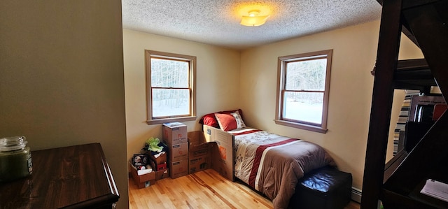bedroom with a baseboard radiator, light wood-type flooring, a textured ceiling, and multiple windows