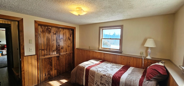 bedroom featuring wood finished floors, a textured ceiling, a closet, wainscoting, and wooden walls