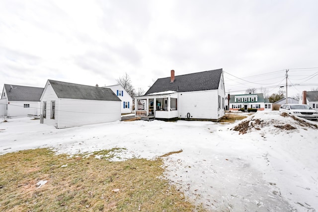 snow covered back of property featuring an outdoor structure and a chimney