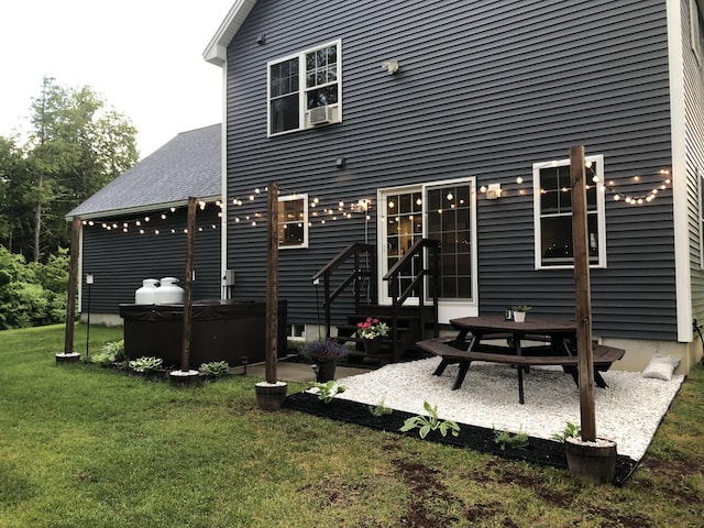 rear view of house featuring a patio, a lawn, roof with shingles, and a hot tub