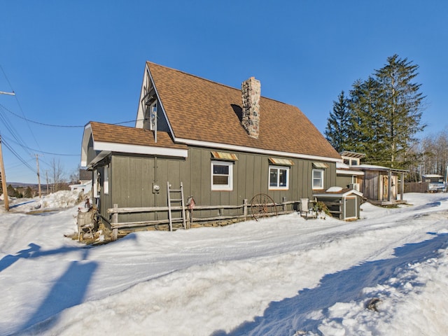 snow covered back of property featuring a chimney and a shingled roof