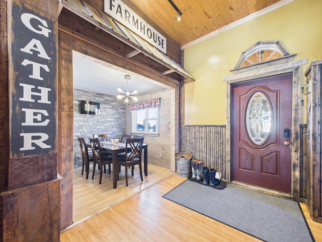 entryway with wood finished floors, ornamental molding, wainscoting, wooden ceiling, and a notable chandelier