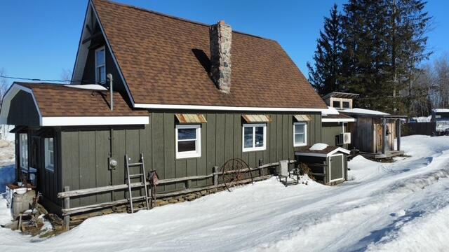 snow covered rear of property with a chimney and roof with shingles