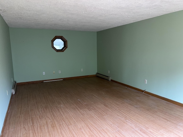 empty room with a baseboard heating unit, wood finished floors, a textured ceiling, baseboard heating, and baseboards