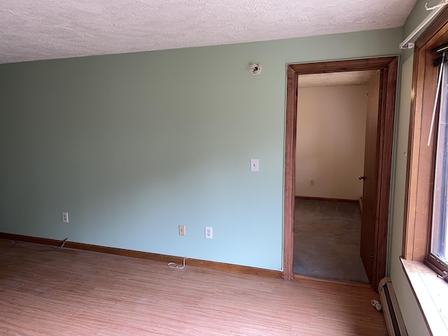 unfurnished room featuring baseboards, baseboard heating, a textured ceiling, and wood finished floors